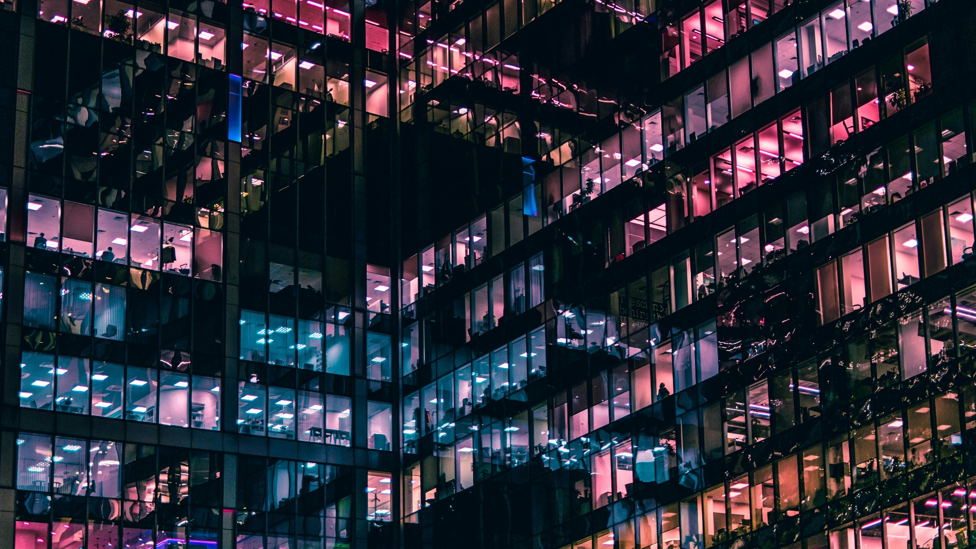 Illuminated office building windows glowing pink and blue at night